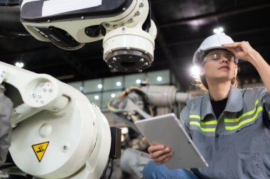 Kadın bir mühendis robot deposundaki robot koluna bir program yüklüyor. Makineyi müşteriye göndermeden önce işlemi test edin.