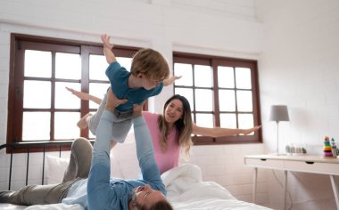 Küçük çocuk babasıyla birlikte uçuyor. Yatak odasında, yatağının üstünden uçmasına yardım etmek için bacaklarını kullanıyor..