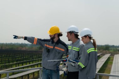 Büyük bir güneş enerjisi depolama istasyonunun çatısında elektrik mühendislerinden oluşan bir ekip yüzlerce dönüm alana kurulmuş güneş panellerini inceliyor..