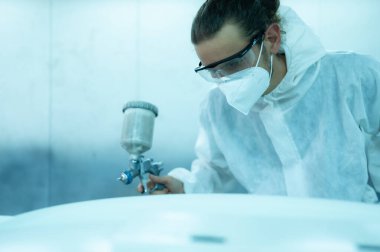 Araba sprey odasındaki oto tamircisi arabanın ön tamponuna püskürtülen boyayı inceliyor. Pigmentin tam, güzel ve arabanın orijinal rengiyle uyumlu olduğunu gösteriyor.