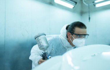 Araba sprey odasındaki oto tamircisi arabanın ön tamponuna püskürtülen boyayı inceliyor. Pigmentin tam, güzel ve arabanın orijinal rengiyle uyumlu olduğunu gösteriyor.