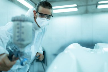 Araba sprey odasındaki oto tamircisi arabanın ön tamponuna sprey püskürtücü enjekte ederek arabanın orijinal rengiyle harmanlanan güzelliği yaratmak için arabanın ön tamponuna incelik katıyor.