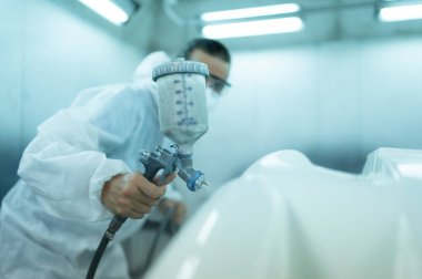 Araba sprey odasındaki oto tamircisi arabanın ön tamponuna sprey püskürtücü enjekte ederek arabanın orijinal rengiyle harmanlanan güzelliği yaratmak için arabanın ön tamponuna incelik katıyor.