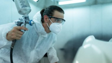 Araba sprey odasındaki oto tamircisi arabanın ön tamponuna püskürtülen boyayı inceliyor. Pigmentin tam, güzel ve arabanın orijinal rengiyle uyumlu olduğunu gösteriyor.