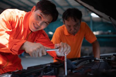 Her iki oto tamircisi de bir garajda tamir için getirilen bir müşterinin arabasının motorunu inceliyor..