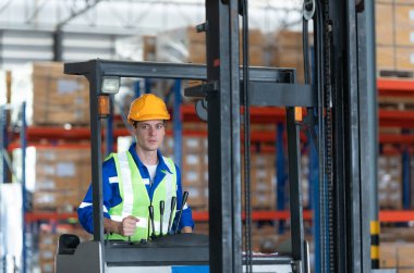 Otomobil parçaları deposunda çalışan işçiler, araba montaj hattına teslim edilmeyi bekleyen deponun deposundaki yedek parça kutusunu getirmek için forklift kullanıyorlar.
