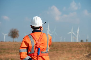 Doğal Enerji Rüzgâr Türbinleri 'nin mühendisi büyük rüzgar türbinlerinin icabına bakmak için rüzgar türbininin tepesinde çalışan bir meslektaşla iletişim kurmak için bir telsiz kullan..