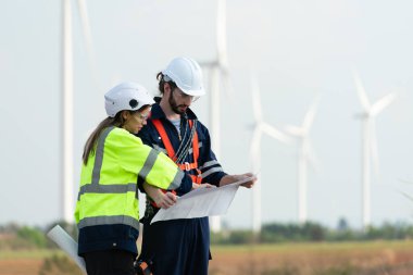Doğal Enerji Rüzgâr Türbini sahasında görevli kadın ve erkek mühendis. Rüzgar enerjisini elektriğe dönüştüren büyük rüzgar türbini operasyonlarının günlük denetim görevleriyle