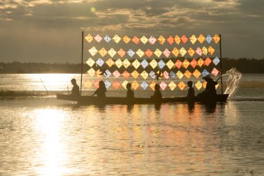 Tayland 'ın kırsal kesimlerinde küçük bir kız bir teknede oturur ve akşam rüzgarına sarılmış, gölün ortasında renkli uçurtmaların tadını çıkarır..