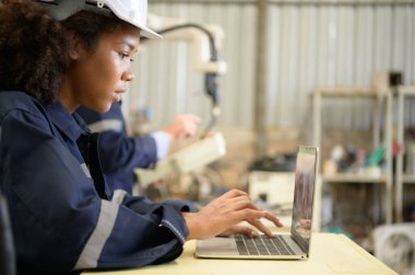 İki mühendis kaynak yapan robotları kontrol ediyor. Birbirlerinin yeteneklerini aktarmaya ve paylaşmaya hazırlar.