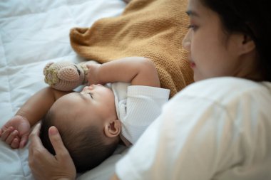 Genç anne, yeni doğmuş bebeğine sarılarak beyaz yatak odasında uyumasını, günün akşamında sıcak güneş ışığını beklemesini ister..