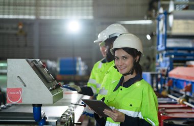 Young female engineer learning to run machinery at a factory with veteran engineers on hand to offer guidance and assistance. clipart