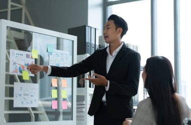 Bir grup genç Asyalı girişimci. Doğal ışık pencereli bir toplantı odasında hisse senedi yatırım verilerini gözden geçirmek için toplantı.