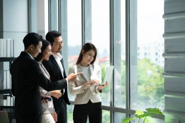 Bir grup genç Asyalı girişimci, gün ışığı pencereli bir toplantı odasında hisse yatırım bilgilerini gözden geçirmek için toplantı düzenliyor..