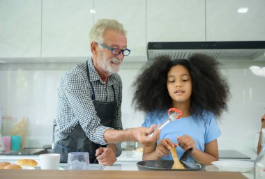 Büyükbaba ve torunlarla aile tatili aktiviteleri. Büyükbaba, yarı Asyalı torunu Afro-Amerikan 'a yemek pişirmeyi öğretiyor.