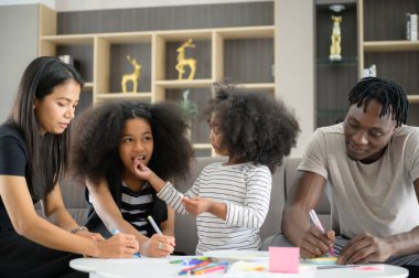 Asyalı-Afrikalı-Amerikalı aile evin oturma odasında dinleniyor, sohbet ediyor, resim yapıyor ve eğleniyor.