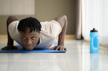 Genç Afrikalı adam, günün sabah atmosferinde hafif sporlarla rahatlama zevkiyle evinin oturma odasında yoga egzersizi yapıyor..