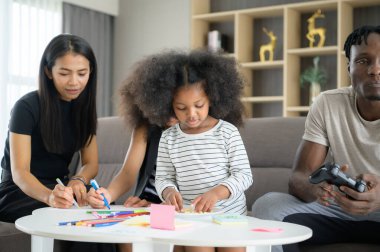 Asyalı-Afrikalı-Amerikalı aile evin oturma odasında dinleniyor, sohbet ediyor, resim yapıyor ve eğleniyor.