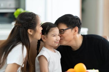 Asyalı anne ve baba, küçük kızınıza sevgilerinizi gösterin ve birlikte kahvaltı edin..