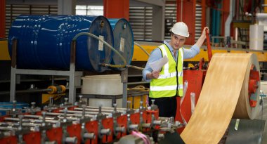 İki genç mühendis, fabrikada metal levha oluşturan makinelerin çalışmasını test ediyor ve doğruluyor.