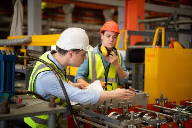 İki genç mühendis, fabrikada metal levha oluşturan makinelerin çalışmasını test ediyor ve doğruluyor.