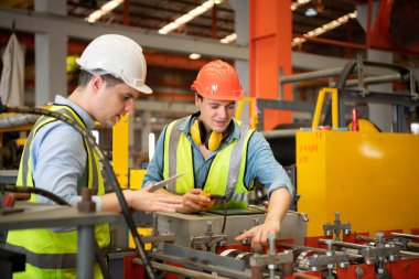 İki genç mühendis, fabrikada metal levha oluşturan makinelerin çalışmasını test ediyor ve doğruluyor.