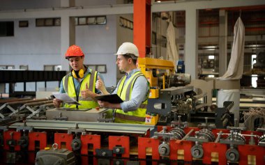 İki genç mühendis, fabrikada metal levha oluşturan makinelerin çalışmasını test ediyor ve doğruluyor.