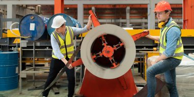 İki genç mühendis, fabrikada metal levha oluşturan makinelerin çalışmasını test ediyor ve doğruluyor.