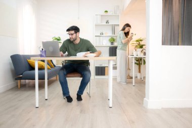 Evde kız arkadaşıyla bilgisayarla çalışırken gülümseyen genç bir serbest çalışanın portresi.