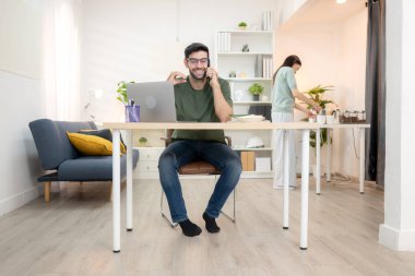 Evde kız arkadaşıyla bilgisayarla çalışırken gülümseyen genç bir serbest çalışanın portresi.