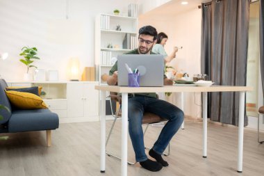 Evde kız arkadaşıyla bilgisayarla çalışırken gülümseyen genç bir serbest çalışanın portresi.