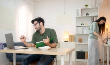 Evde kız arkadaşıyla bilgisayarla çalışırken gülümseyen genç bir serbest çalışanın portresi.