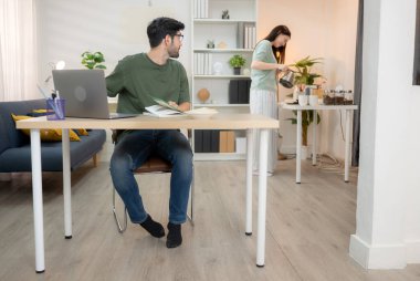 Evde kız arkadaşıyla bilgisayarla çalışırken gülümseyen genç bir serbest çalışanın portresi.