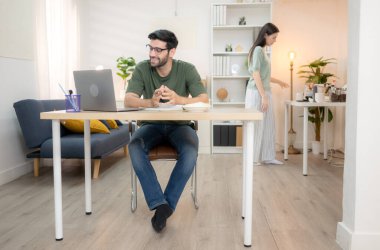 Evde kız arkadaşıyla bilgisayarla çalışırken gülümseyen genç bir serbest çalışanın portresi.