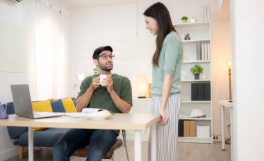 Evde kız arkadaşıyla bilgisayarla çalışırken gülümseyen genç bir serbest çalışanın portresi.