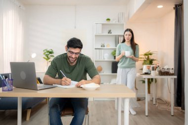 Evde kız arkadaşıyla bilgisayarla çalışırken gülümseyen genç bir serbest çalışanın portresi.