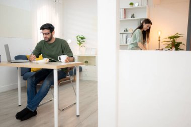 Evde kız arkadaşıyla bilgisayarla çalışırken gülümseyen genç bir serbest çalışanın portresi.