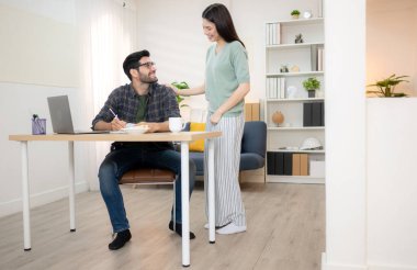 Evde kız arkadaşıyla bilgisayarla çalışırken gülümseyen genç bir serbest çalışanın portresi.