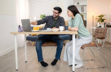 Evde kız arkadaşıyla bilgisayarla çalışırken gülümseyen genç bir serbest çalışanın portresi.