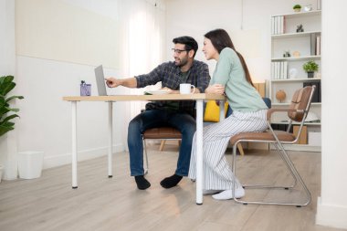 Evde kız arkadaşıyla bilgisayarla çalışırken gülümseyen genç bir serbest çalışanın portresi.