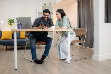 Evde kız arkadaşıyla bilgisayarla çalışırken gülümseyen genç bir serbest çalışanın portresi.