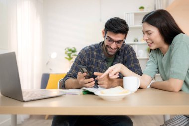Evde kız arkadaşıyla bilgisayarla çalışırken gülümseyen genç bir serbest çalışanın portresi.