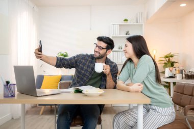 Evde kız arkadaşıyla bilgisayarla çalışırken gülümseyen genç bir serbest çalışanın portresi.