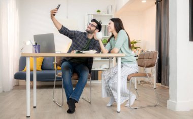 Evde kız arkadaşıyla bilgisayarla çalışırken gülümseyen genç bir serbest çalışanın portresi.