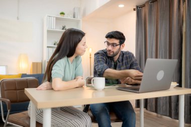 Evde kız arkadaşıyla bilgisayarla çalışırken gülümseyen genç bir serbest çalışanın portresi.