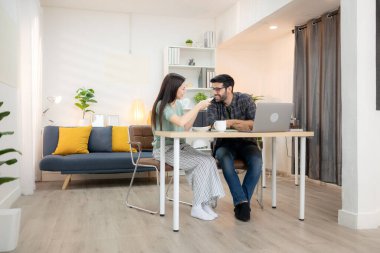 Evde kız arkadaşıyla bilgisayarla çalışırken gülümseyen genç bir serbest çalışanın portresi.