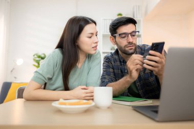 Evde kız arkadaşıyla bilgisayarla çalışırken gülümseyen genç bir serbest çalışanın portresi.