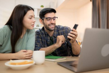 Evde kız arkadaşıyla bilgisayarla çalışırken gülümseyen genç bir serbest çalışanın portresi.