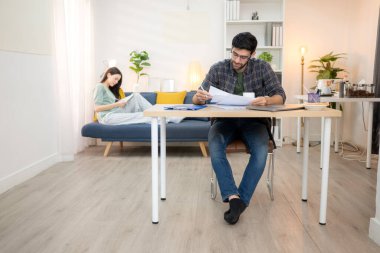 Evde kız arkadaşıyla bilgisayarla çalışırken gülümseyen genç bir serbest çalışanın portresi.