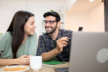 Evde kız arkadaşıyla bilgisayarla çalışırken gülümseyen genç bir serbest çalışanın portresi.